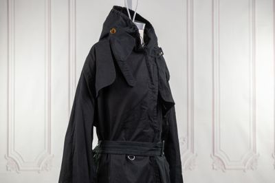 une photo d'un trench-coat noir accroché à un mur blanc