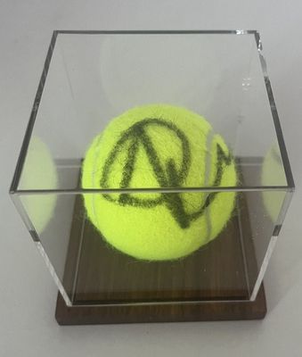 une balle de tennis jaune dans une boîte transparente sur laquelle figurent des inscriptions