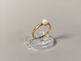 une bague en or sertie d'une perle, posée sur un socle transparent
