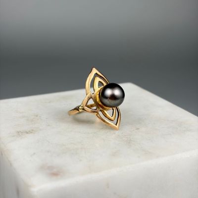 une photo d'une perle noire et d'une bague en or posées sur un bloc de marbre