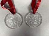 two silver christmas ornaments with red ribbon on a white surface