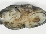 un objet en pierre sur lequel est représenté un poisson, posé sur une surface blanche