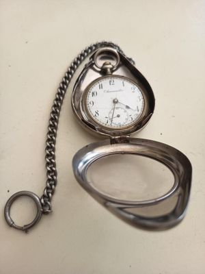 une montre de poche en argent posée sur une table, entourée d'une chaîne