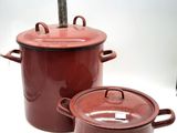 Deux pots rouges munis d'anses sont posés sur une surface blanche.