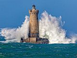 a lighthouse in the middle of the ocean with a big wave crashing on it