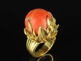 an image of a gold ring with a coral stone surrounded by leaves