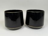 deux tasses noires aux bords dorés posées sur un fond blanc