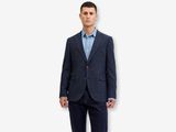 a man in a suit standing against a white wall
