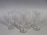 six clear wine glasses are lined up on a white surface