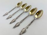 four spoons with a gold handle are lined up on a white surface