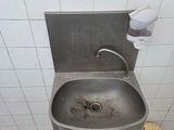 a dirty sink in a public restroom with a toilet paper dispenser