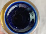 a hand holding a blue glass with a gold rim