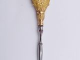 a gold spoon with a metal handle on a white surface
