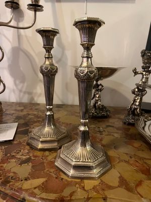 two silver candlesticks on a table with a picture on the wall in the background