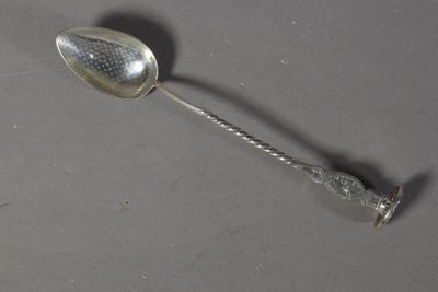 une cuillère en argent avec un manche, posée sur une surface grise