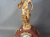 une statue en or représentant une femme tenant un oiseau sur une horloge rouge
