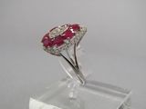 une photo d'une bague sertie d'un diamant et d'un rubis, posée sur un socle transparent