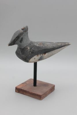 l'image d'un oiseau posé sur un socle en bois, sur fond blanc