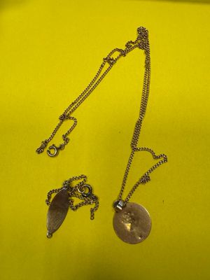 deux colliers en argent posés sur un tissu jaune