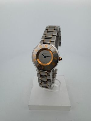une photo d'une montre-bracelet argentée et dorée posée sur un socle blanc