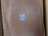 un livre marron dans une boîte marron ornée d'un emblème bleu