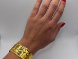 woman ' s hand with red manicured nails and gold cuff bracelet