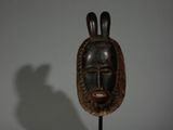 une image représentant un masque en bois posé sur un socle, sur fond blanc
