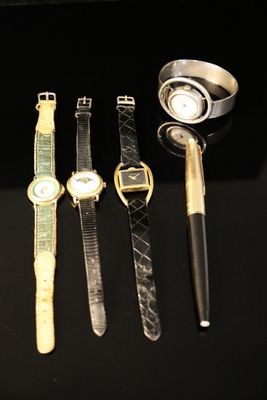 four different watches and a pen are sitting on a black surface