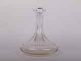 une carafe en verre transparent posée sur une surface blanche, avec un fond blanc
