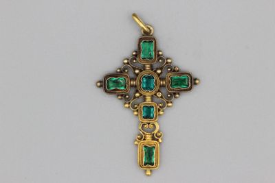 un gros plan d'une croix en or ornée de pierres vertes