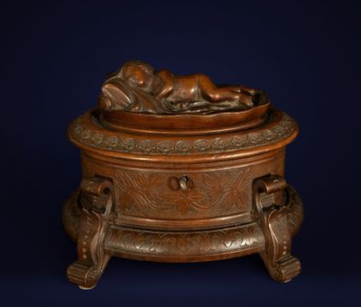 une boîte ancienne en bronze, posée sur un socle, contenant un bébé
