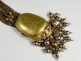 a necklace with a gold beetle on it on a white surface