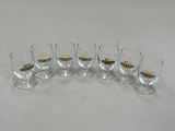 six verres aux bords dorés sont alignés sur une surface blanche