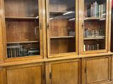 une grande bibliothèque en bois avec des portes vitrées dans une pièce