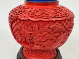 a red vase with a blue lid sitting on a stand