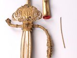 a gold colored sword with a red handle on a white surface