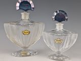 une paire de flacons de parfum en verre posés sur une surface blanche