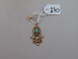 un gros plan sur une petite main de Hamsa en or ornée d'une pierre turquoise