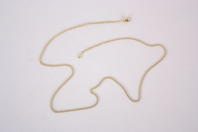 un gros plan d'un collier avec une chaîne en or posé sur une surface blanche