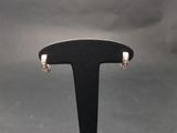 un gros plan sur une paire de boucles d'oreilles créoles en argent posées sur un support noir