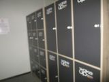 Plusieurs casiers noirs sont alignés dans une pièce où est accrochée une affiche au mur