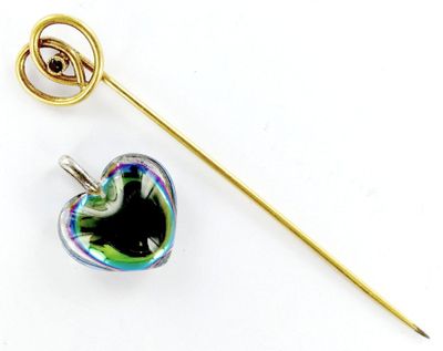 une broche en forme de cœur et un bâton posés sur une surface blanche