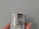 someone is holding a silver cup in their hand on a gray background