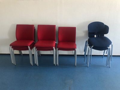 Quatre chaises rouges sont alignées contre un mur blanc dans une salle d'attente