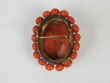 a close up of a broochle with orange beads on a white surface