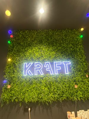 L'enseigne au néon de Kraff devant un mur de plantes vertes
