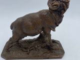 bronze statue of a ram standing on a rock on a white background
