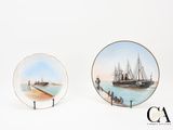 two plates with paintings of ships on them sitting on a white surface