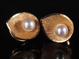 une paire de boucles d'oreilles en or et perles posées sur un fond noir
