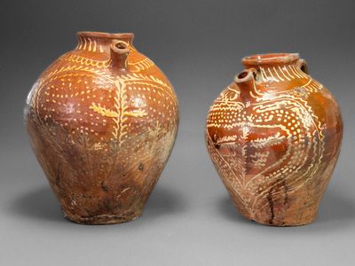 two brown vases with designs on them sitting side by side